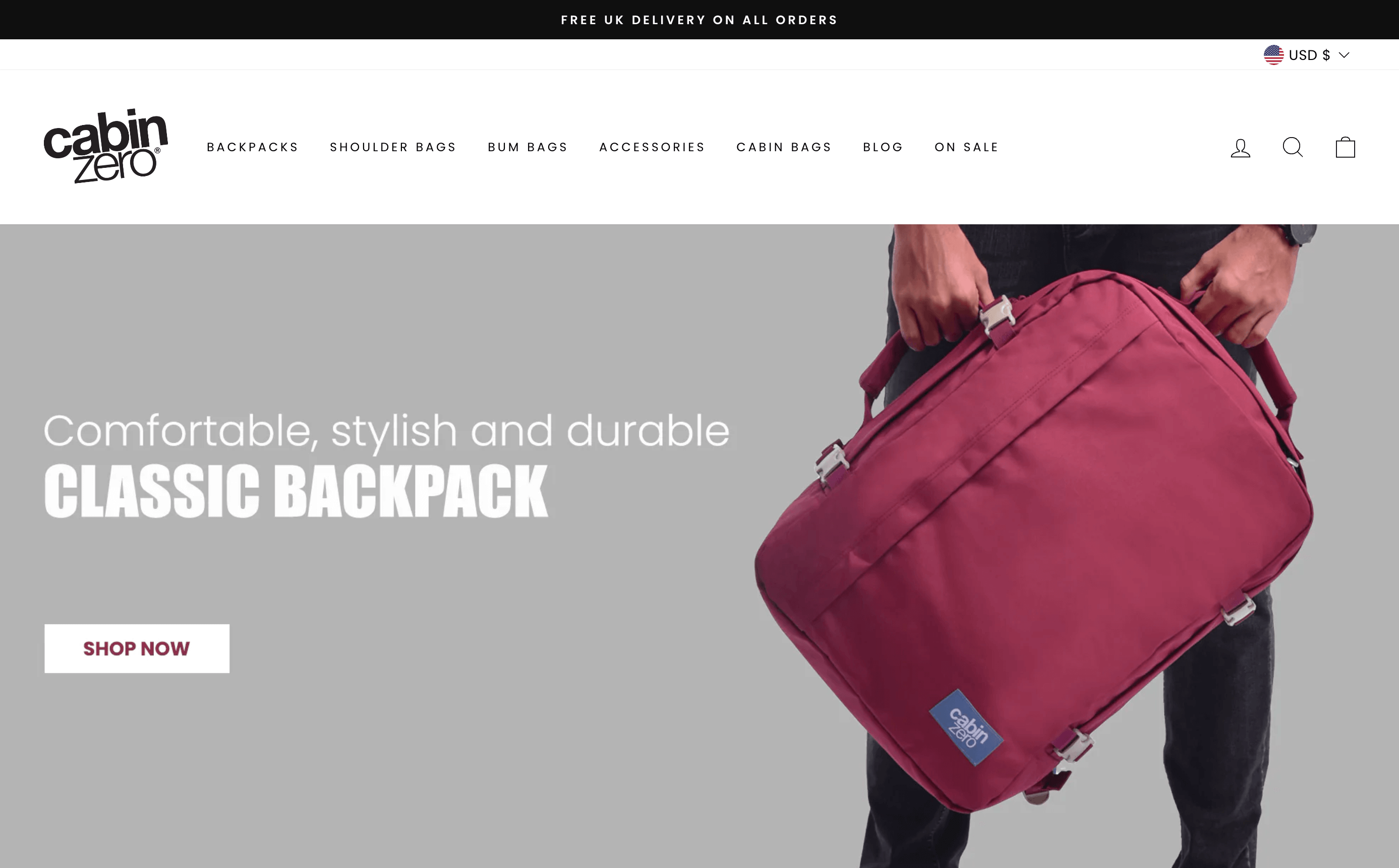 Storytelling Brands–Cabin Zero’s homepage shows a banner image of a man holding one of its red travel backpacks. There is a CTA to shop their Classic Backpack range of products. 