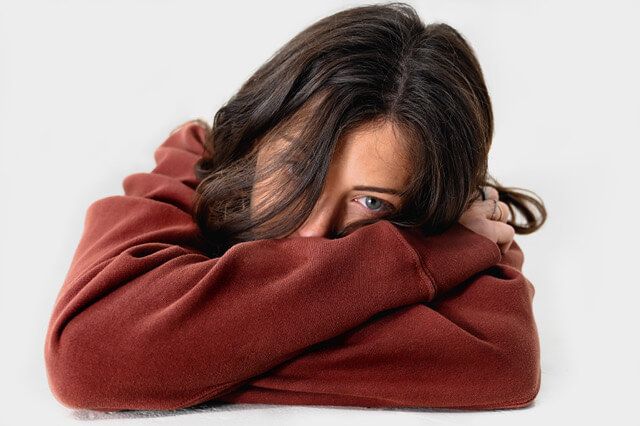 A headshot of the founder and CEO of XIVI, Taylor Hertz. She has long brunette hair with blue eyes and is wearing a maroon hoodie. She has her arms crossed on a table and is resting her head on them, partially covering her face.