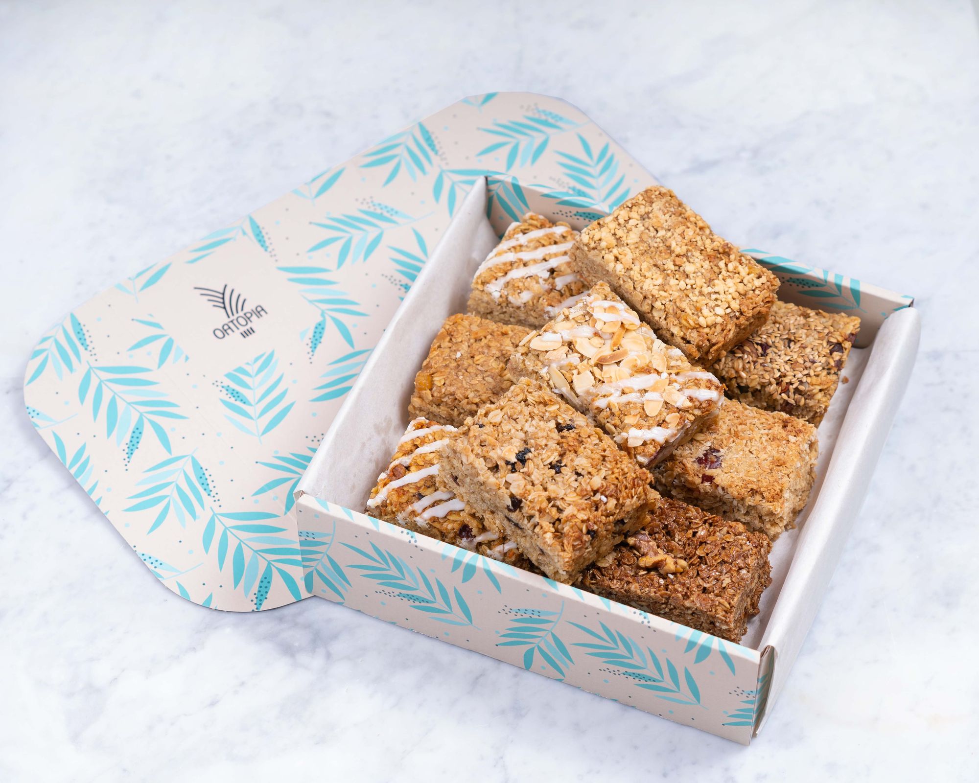 A bird’s eye view image of a branded Oatopia box full of oat-based flapjacks. There are different varieties with frosting, berries, nuts, and other ingredients in them. 