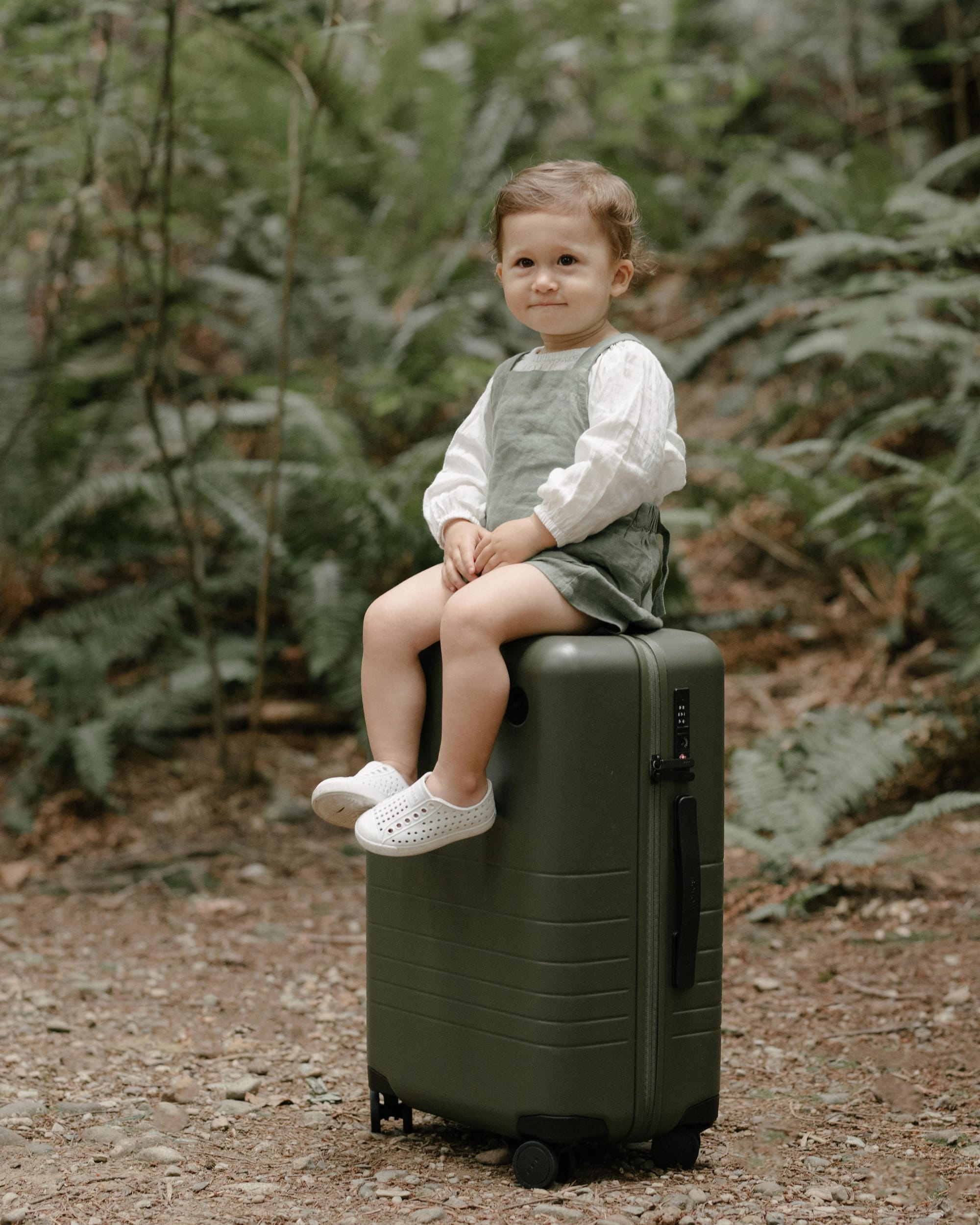 picture of a little one year old kid on top of a monos luggage outside